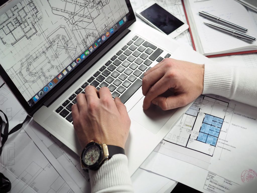 Man Using Turned-on Macbook Pro on White Printer Papers